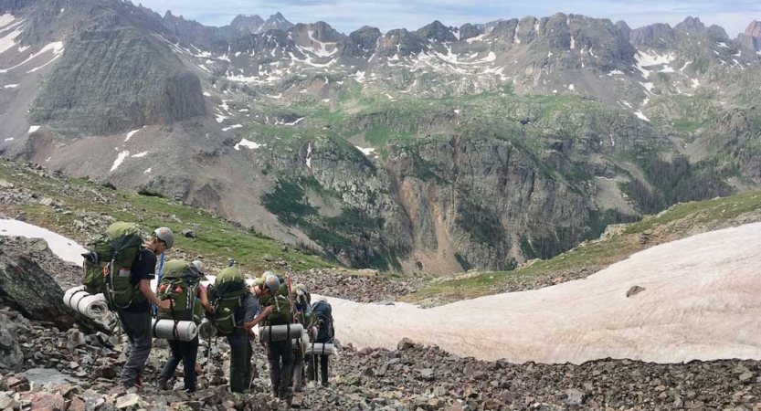 A group of backpackers descend into a mountainous valley. 